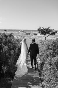 Bride and Groom walk down boardwalk towards Atlantic Ocean during wedding on Nantucket.
