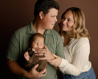 Father holding his sleeping newborn baby while the mother lovingly looks at them during a warm lifestyle newborn portrait session by Kaitlyn Dawn Photography.