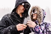 A couple toasts champagne while wearing ski attire after getting engaged on the snowy Copper Mountain by Jackelynn Noel Photography.