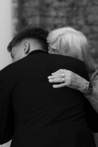 A raw and heartwarming documentary shot of a grandmother hugging her grandson, the groom, during an emotional wedding day.