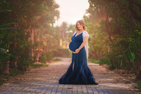 Expecting mother in navy blue gown standing on garden path during golden hour maternity session