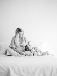 Black and white image of a toddler girl laying on her mom's legs and looking up at her.