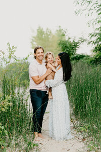 family together on the beach in tall grass by the lake michigan smiling at camera