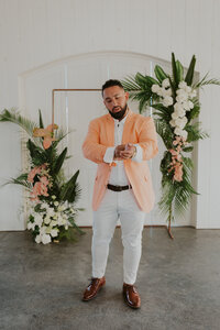 Groom getting ready for his wedding day in front of tropical summer floral archway