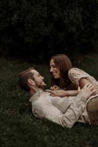 A couple rolls together in the grass, cozy and laughing during their engagement photoshoot in New England. Fine art lifestyle photography capturing romantic, intimate, and playful moments.