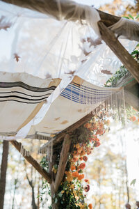 A close-up of the chuppah canopy, featuring a traditional tallit with blue and black stripes and delicate fringe