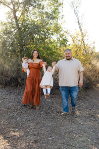 Family walking hand in hand along a wooded path during golden hour, relaxed and candid outdoor family photography by Kaitlyn Dawn Photography.