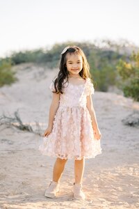 Young girl from the Collins family smiling in a blush pink dress in the Las Vegas desert during a golden hour children’s portrait session.