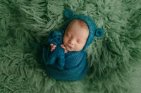 Newborn baby wrapped in deep teal and green with matching knit bear toy, captured at a fine art newborn studio serving Waukesha, Pewaukee, and Oconomowoc