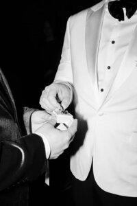 Candid shot of a groom in a stylish white tuxedo receiving wedding rings from the best man during the ceremony.
