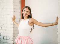 Senior portrait in downtown Foley, Alabama — hands pressed on a weathered brick doorway,
wearing a white top and pink skirt.