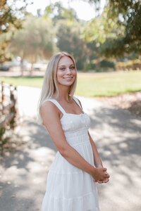 senior girl with her hands clasped and smiling at the camera at Sharon Park, Menlo Park