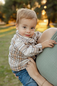 Close-up of a toddler boy holding onto his mother in warm golden hour light, candid child portrait by Kaitlyn Dawn Photography.