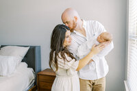 Dad cradles baby as he leans over to kiss mom during lifestyle newborn session in Propser, TX with Mckinney newborn photographer Ling Waters Photography