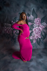 Pregnant woman in a hot pink gown posing with hand on hip against a floral backdrop during a Cleveland maternity photography session