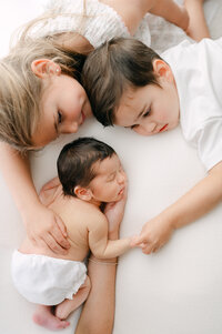 Siblings holding their baby sister's hand