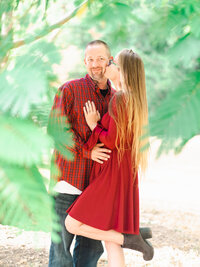 Couple wearing red outfits during a Christmas engagement photo session in a Los Angeles park with festive holiday vibes.