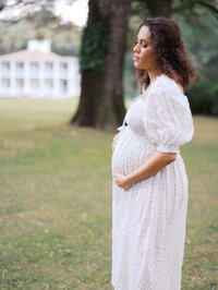 Pregnant mom in a white flowy gown standing in a field in Seattle with her eyes closed