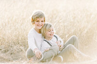 Little brothers sitting together in the middle of a grassy field in Dallas.