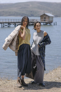 Two models in layered knitwear, a puffer and a flannel overshirt on the shoreline, styled for MUJI's AW26 lookbook