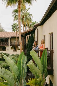Two guests talking on a guest room balcony above the palms