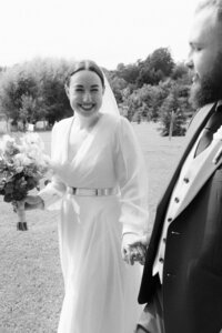Joyful bride laughing at the camera while walking hand in hand with the groom through the streets of Prague.