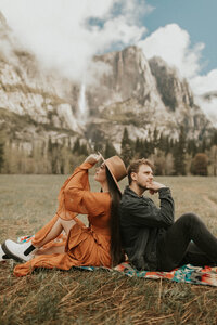 man and woman sitting on blanket in front of mountainscape