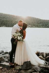 A bride and groom embrace one another in a kiss in front of a lake