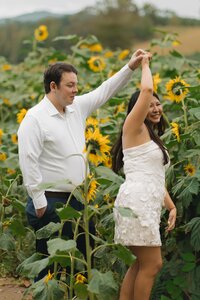 Engaged couple twirling in the sunflower fields at Fausett Farms Sunflowers in Dawson County, Georgia, surrounded by vibrant yellow blooms during their engagement photo session