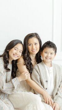 A mother and her two kids sitting on a bench inside of a Dallas/Fort Worth photography studio as they all look and smile at the photographer.