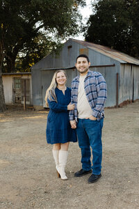 Couple standing together in front of a rustic barn, coordinated outfits and natural outdoor lighting captured by Kaitlyn Dawn Photography, professional family and couple’s portrait photographer.