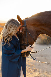 High school graduate wearing a cap and gown gently holding a horse in warm sunset light, senior portrait by Kaitlyn Dawn Photography.