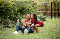 Sibling chaos in full force during a Jacksonville family photography session with Nature’s Child Photography as little sister launches a surprise cheek kiss and her brother completely loses it laughing in the grass.