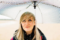 Kelly from Paul Joseph photography smiling whilst stood under an umbrella on a rainy day.