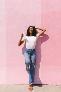 Full-length lifestyle frame against a pink stucco wall, beauty campaign photography