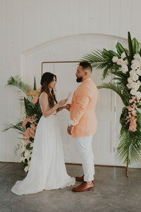 Bride and groom exchange their vows at their wedding ceremony in front of a stunning tropical floral wedding arch