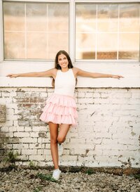 Senior portrait in downtown Foley, Alabama — arms resting on a windowsill above a weathered
white brick wall.