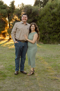 Couple embracing in a sunlit field with trees in the background, romantic lifestyle portrait photographed by Kaitlyn Dawn Photography.