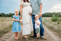 Pregnant Mom, dad, and 2 kids standing on dirt road.