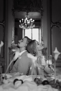 Couple dos à dos, yeux fermés, dans un salon élégant orné d'un lustre à pampilles et de miroirs dorés, portrait éditorial en noir et blanc