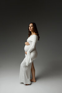Expecting mom in a fitted white maternity gown posing in profile, highlighting her pregnancy during a Yucaipa session with Kaitlyn Dawn Photography.