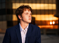 Senior portrait in downtown Mobile, Alabama— closeup headshot wearing the blue dress suit with the sunset shining in the building behind.