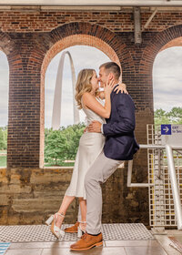 St. Louis engagement photo—couple kissing under brick arches with the Gateway Arch in the background