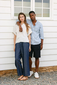 Two models in linen against white horizontal siding, seasonal lookbook frame