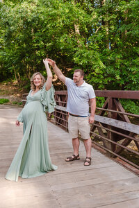 Expectant couple celebrating together on a wooden bridge, wife in a sage green gown, during a Youngstown maternity photography session