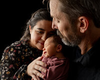 Parents cuddling their sleeping newborn baby during an intimate studio newborn photography session with a dark background in Inland Empire by Kaitlyn Dawn Photography.