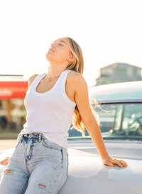 Senior portrait at Sunliner Diner in Gulf Shores, Alabama — leaning against the trunk of a teal
classic car, eyes closed in the sun.