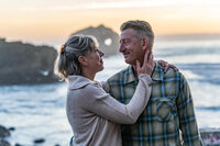 man and woman looking at each other lovingly on the beach at sunset