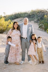The Collins family smiling together in the Las Vegas desert, with parents standing in the center and their three children gathered closely around them during a warm, natural light family portrait session.