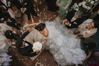 Vue aérienne d’une mariée entrant avec son bouquet, entourée de ses proches qui la célèbrent, robe volumineuse et pétales au sol — instant capturé par un photographe de mariage à Montréal, soulignant l’émotion, l’élégance et la joie du moment.